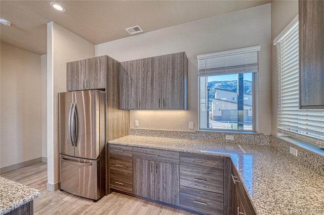 kitchen featuring light stone counters, stainless steel fridge, and light wood-type flooring