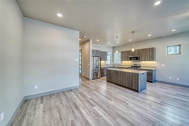 kitchen with sink, hanging light fixtures, stainless steel appliances, a center island, and light wood-type flooring