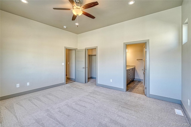 unfurnished bedroom with connected bathroom, a spacious closet, light carpet, a closet, and ceiling fan