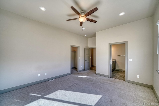 unfurnished bedroom with a walk in closet, carpet floors, ensuite bath, and ceiling fan