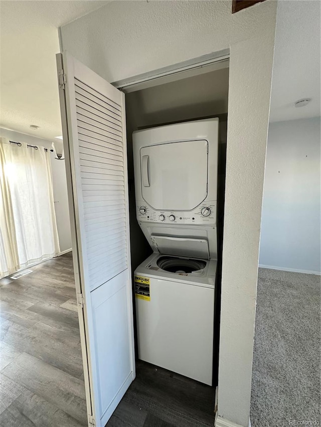 clothes washing area featuring a textured ceiling, wood-type flooring, and stacked washer / dryer