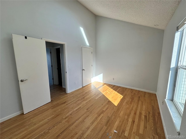 unfurnished room featuring a textured ceiling, light hardwood / wood-style floors, high vaulted ceiling, and a healthy amount of sunlight