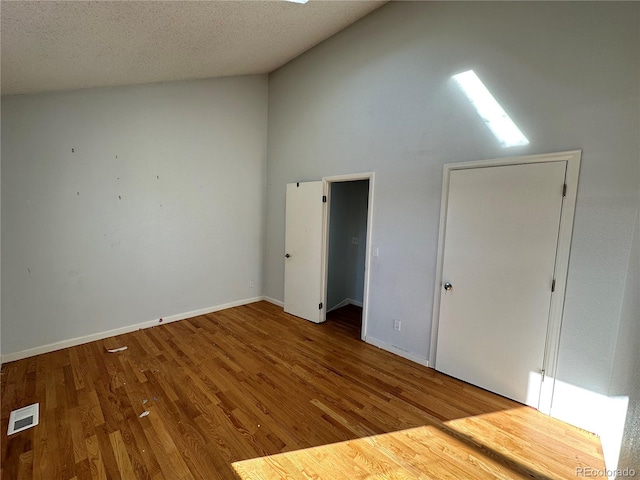 unfurnished bedroom featuring a skylight, hardwood / wood-style floors, high vaulted ceiling, and a textured ceiling