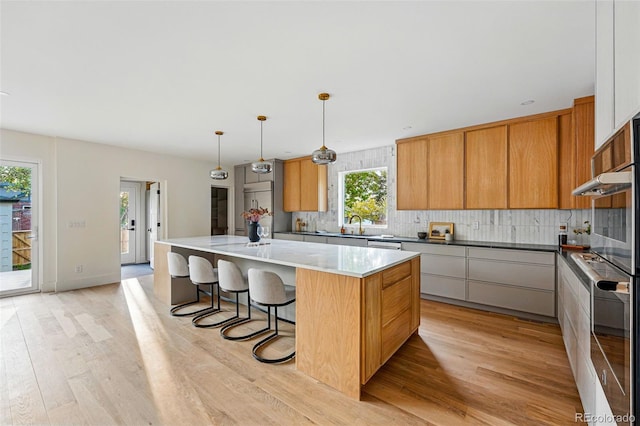 2391 Hudson St, Denver, CO 80207 - kitchen with light wood-style flooring, a kitchen island, backsplash, a breakfast bar area, and stainless steel appliances