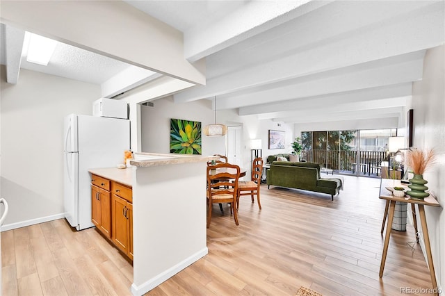 kitchen featuring beamed ceiling, freestanding refrigerator, light wood-style floors, brown cabinetry, and light countertops