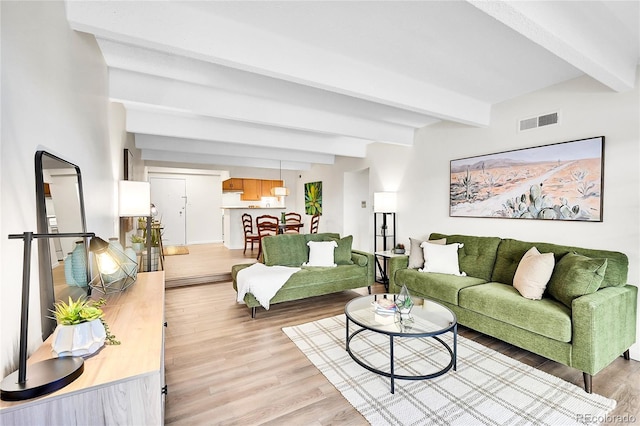 living area with visible vents, beamed ceiling, and light wood finished floors