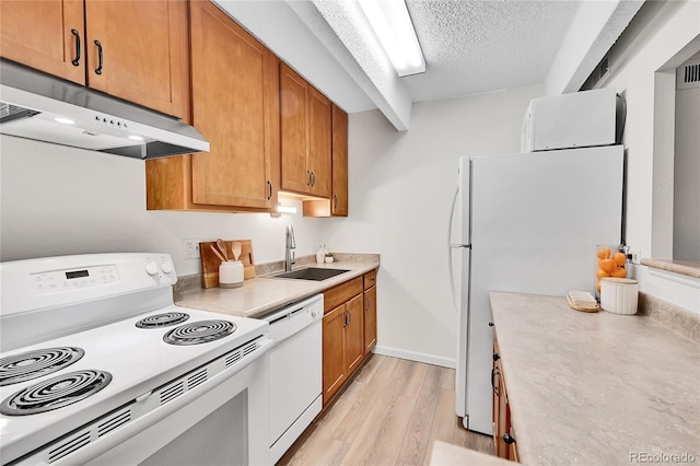 kitchen featuring under cabinet range hood, light countertops, light wood-style flooring, white appliances, and a sink