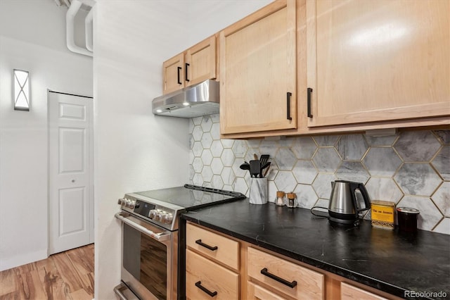 kitchen with dark countertops, under cabinet range hood, light brown cabinetry, light wood-type flooring, and stainless steel range with electric cooktop