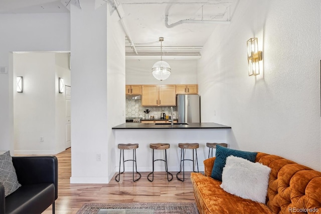 kitchen with stainless steel appliances, light brown cabinetry, light wood-type flooring, and tasteful backsplash