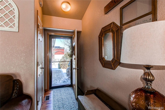 doorway to outside with visible vents, wood finished floors, and a textured wall