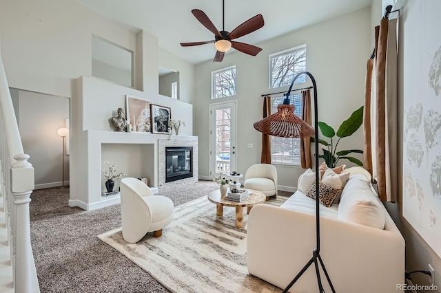 living area with baseboards, a ceiling fan, a glass covered fireplace, a towering ceiling, and carpet floors