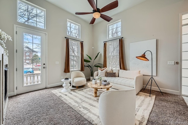 living area featuring carpet flooring, baseboards, ceiling fan, and a high ceiling