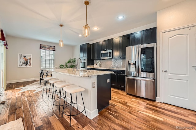 kitchen featuring stainless steel appliances, dark cabinetry, backsplash, and a kitchen breakfast bar