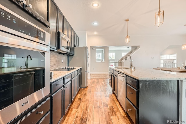 kitchen with stainless steel appliances, a sink, light wood-type flooring, backsplash, and pendant lighting