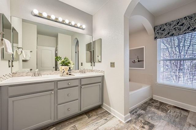 full bathroom featuring double vanity, baseboards, visible vents, a garden tub, and a sink