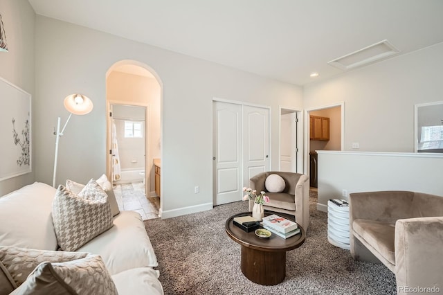 living area featuring attic access, arched walkways, baseboards, and light colored carpet