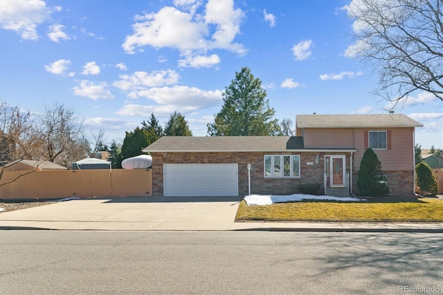 tri-level home with stone siding, driveway, an attached garage, and fence