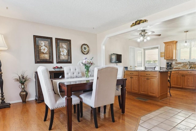 dining area featuring baseboards, ceiling fan, a textured ceiling, and light wood finished floors