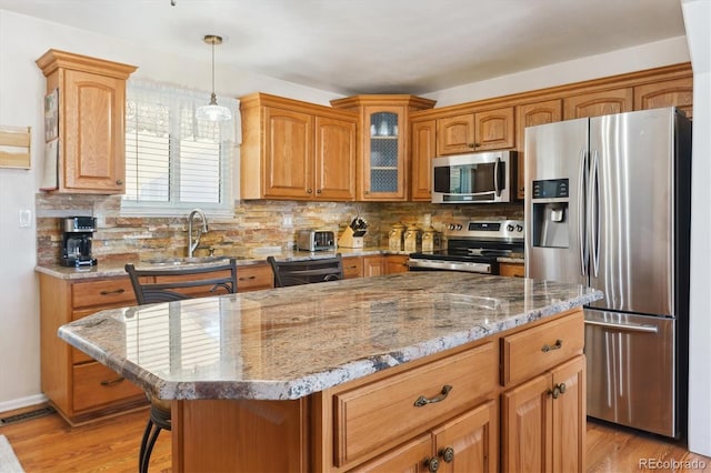 kitchen with light stone counters, appliances with stainless steel finishes, a center island, a sink, and backsplash