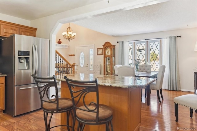 kitchen featuring a center island, brown cabinets, a breakfast bar area, light wood-style flooring, and stainless steel fridge with ice dispenser