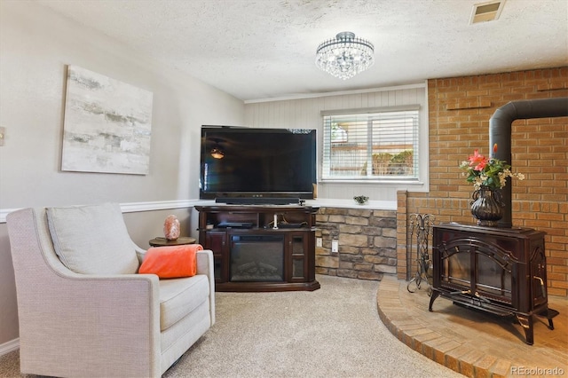 living room featuring a textured ceiling, visible vents, carpet, a glass covered fireplace, and a wood stove