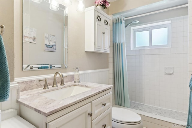 bathroom with toilet, a stall shower, vanity, and wainscoting