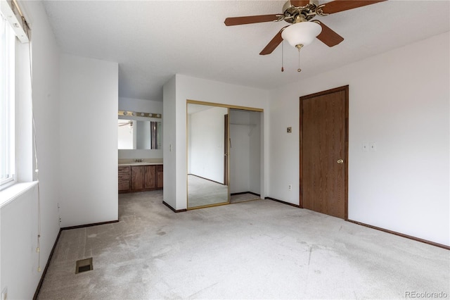 unfurnished bedroom featuring light carpet, a closet, ceiling fan, and ensuite bath