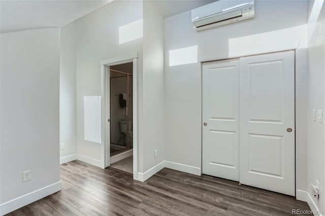 unfurnished bedroom featuring ensuite bath, a closet, dark hardwood / wood-style flooring, and a wall mounted air conditioner