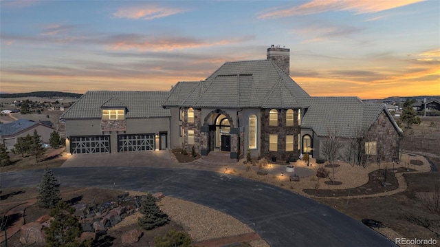 french provincial home with stone siding, driveway, and a tiled roof