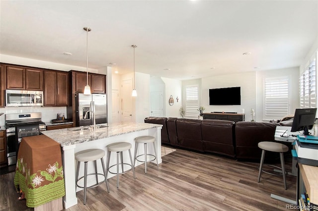 kitchen featuring a kitchen bar, stainless steel appliances, wood-type flooring, decorative light fixtures, and an island with sink