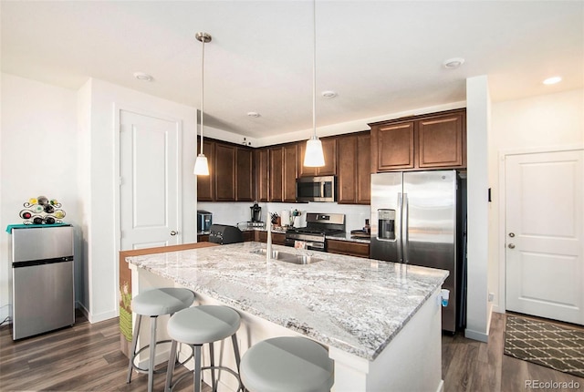 kitchen with dark hardwood / wood-style flooring, an island with sink, stainless steel appliances, and decorative light fixtures