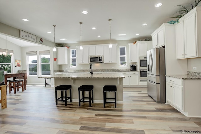 kitchen with stainless steel appliances, a sink, white cabinets, light wood finished floors, and recessed lighting