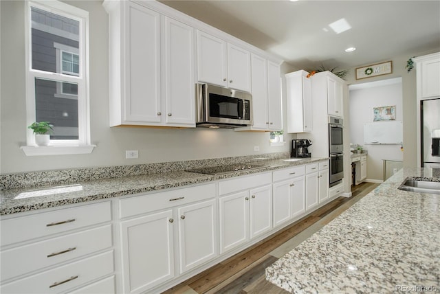 kitchen featuring appliances with stainless steel finishes, white cabinetry, light wood finished floors, light stone counters, and recessed lighting