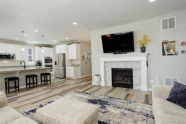 living area featuring light wood-style flooring, recessed lighting, a tiled fireplace, and baseboards