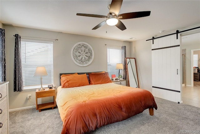 carpeted bedroom with a barn door, baseboards, and a ceiling fan