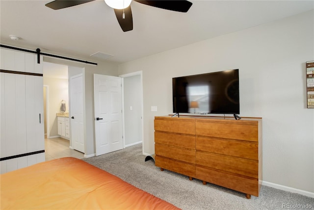 carpeted bedroom featuring baseboards, ensuite bathroom, a barn door, and ceiling fan