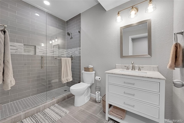 bathroom with toilet, a shower stall, vanity, a textured wall, and baseboards