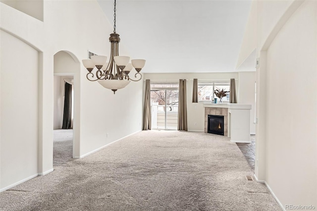 unfurnished living room with a tiled fireplace, a high ceiling, carpet floors, and a notable chandelier