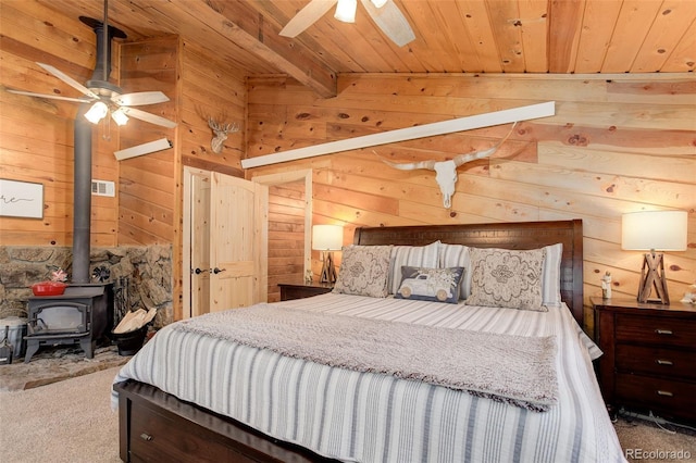 28251 Shadow Mountain Dr, Conifer, CO 80433 - carpeted bedroom featuring wooden ceiling with exposed beams, wooden walls, a wood stove, and ceiling fan