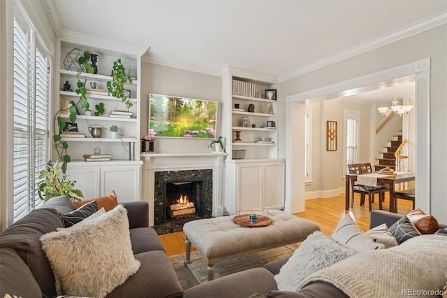 living area with ornamental molding, light wood-type flooring, a fireplace, and a notable chandelier