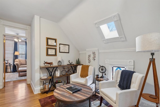 living area with vaulted ceiling with skylight, baseboards, and wood finished floors