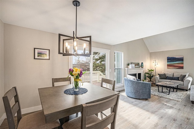 dining area featuring a chandelier, a fireplace, baseboards, vaulted ceiling, and light wood-style floors