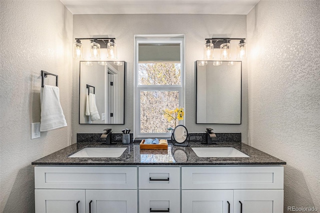 bathroom featuring a textured wall, a sink, and double vanity