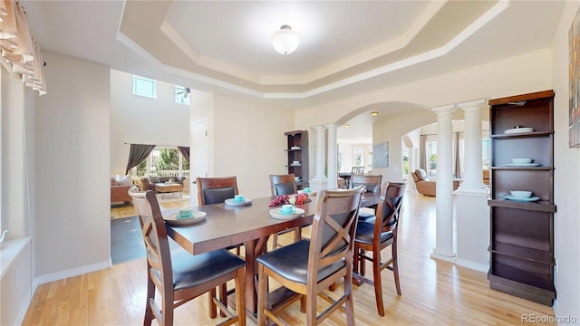 9353 E 146th Ave, Brighton, CO 80602 - dining area featuring decorative columns, a tray ceiling, light wood-style floors, and arched walkways