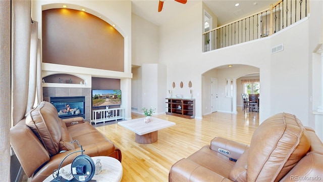 9353 E 146th Ave, Brighton, CO 80602 - living room with arched walkways, wood finished floors, a ceiling fan, a tiled fireplace, and a towering ceiling