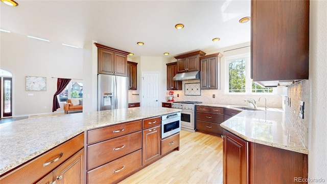 9353 E 146th Ave, Brighton, CO 80602 - kitchen featuring stainless steel appliances, under cabinet range hood, light stone counters, decorative backsplash, and light wood-style floors