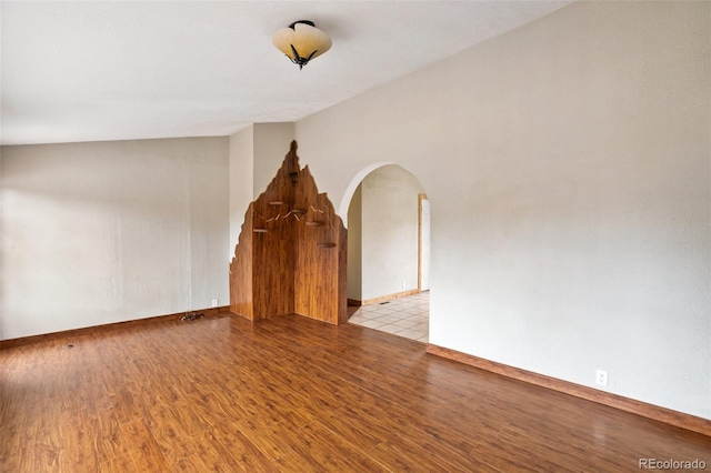 unfurnished living room with wood finished floors, arched walkways, and baseboards