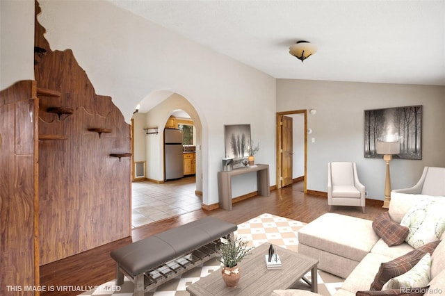 living room with vaulted ceiling, arched walkways, light wood-type flooring, and baseboards