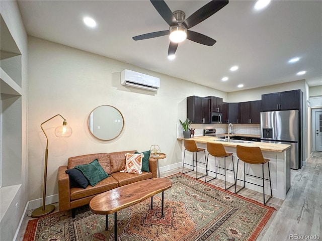 living area featuring light wood finished floors, baseboards, a ceiling fan, a wall mounted air conditioner, and recessed lighting