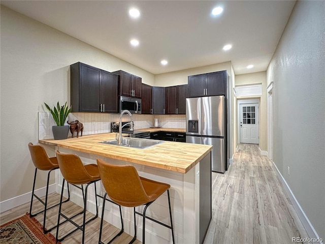 kitchen with a breakfast bar, stainless steel appliances, backsplash, a sink, and a peninsula